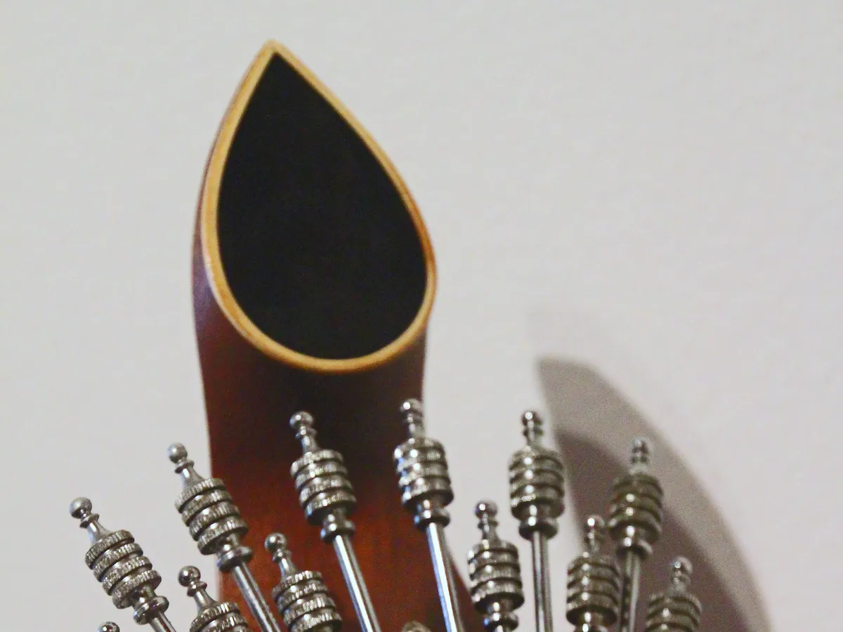 The headstock of a Coimbra guitar, with a teardrop-shaped top and a fan of steel tuning keys