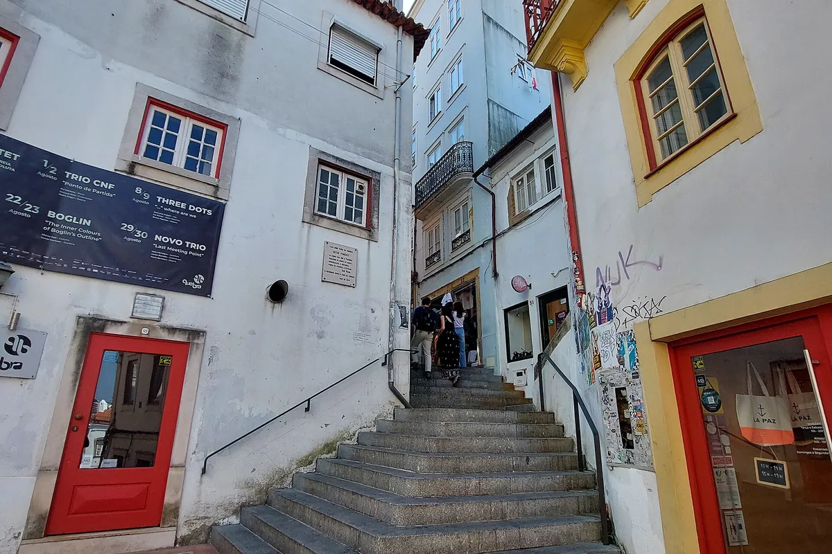 A flight of stone steps climbs between white and yellow houses with red doors on Rua de Quebra-Costas